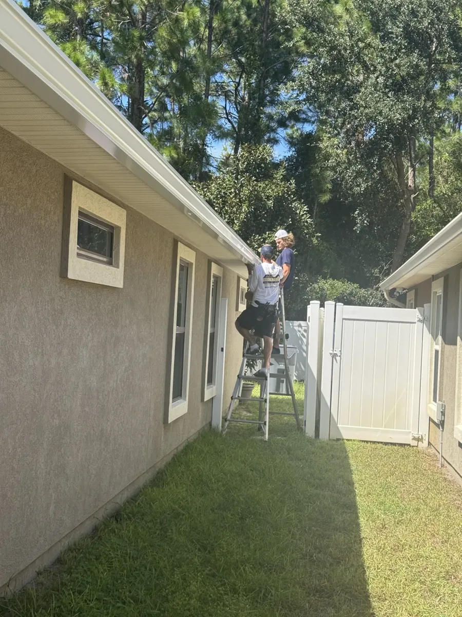 LePierre Roofing gutter installer working from a ladder in a side yard